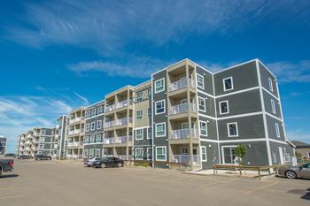 A large grey apartment building with a parking lot in front.